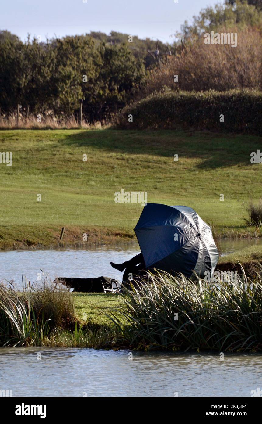 solitary man sitting under fishing umbrella beside lake kent england Stock Photo