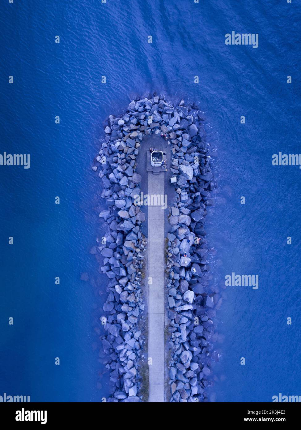 An aerial top view of a pier with wave breakers by sides and blue water