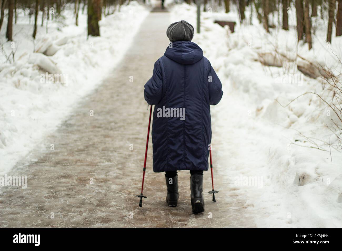 Granny with walking poles in winter. Retired woman. Pensioner walks through park. Healthy walking. Stock Photo
