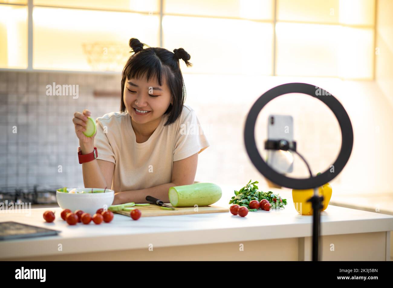 Cheerful cooking vlogger live-streaming her video blog to followers Stock Photo