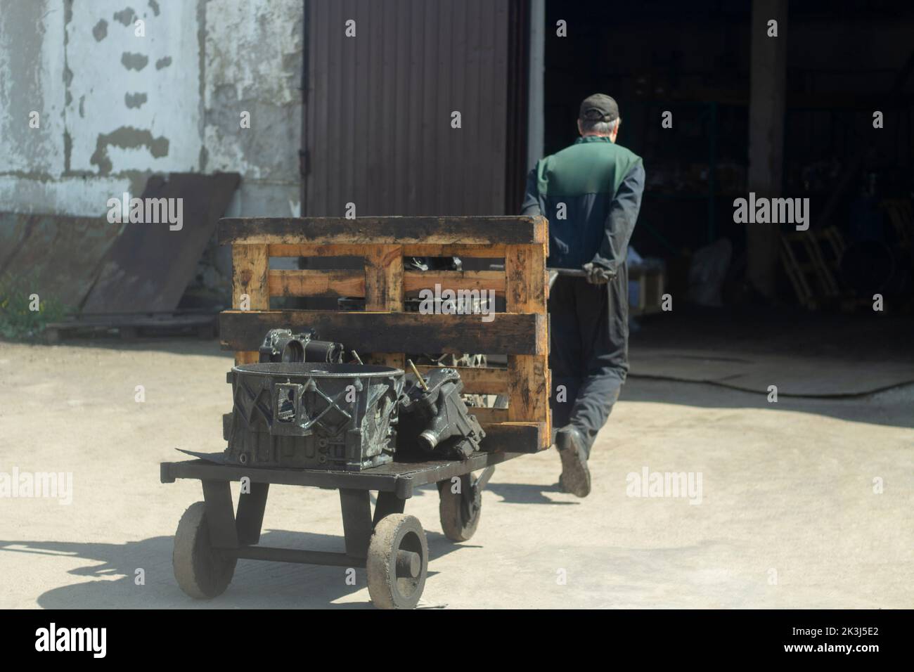 Man carries cart. Worker pulls load. Forklift on street. Man drags vehicle. Stock Photo