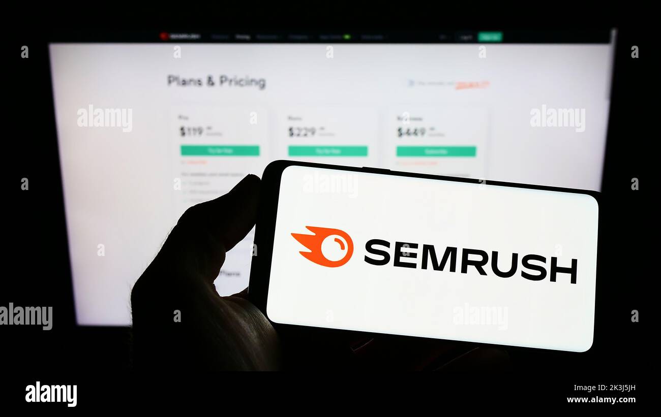 Person holding cellphone with logo of American search engine marketing company SEMrush Inc. on screen in front of web page. Focus on phone display. Stock Photo