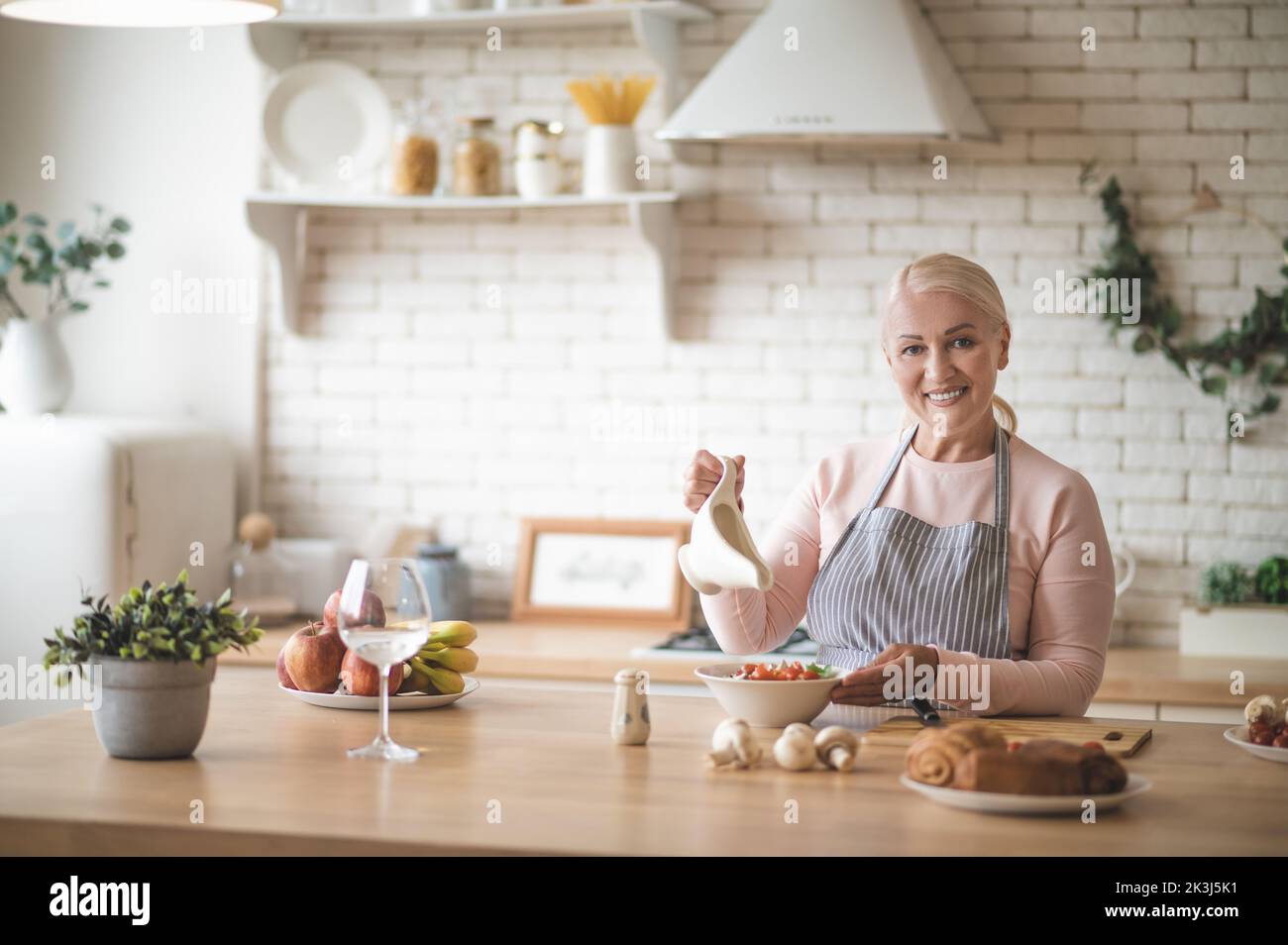 Happy mature lady in the apron dressing the salad Stock Photo