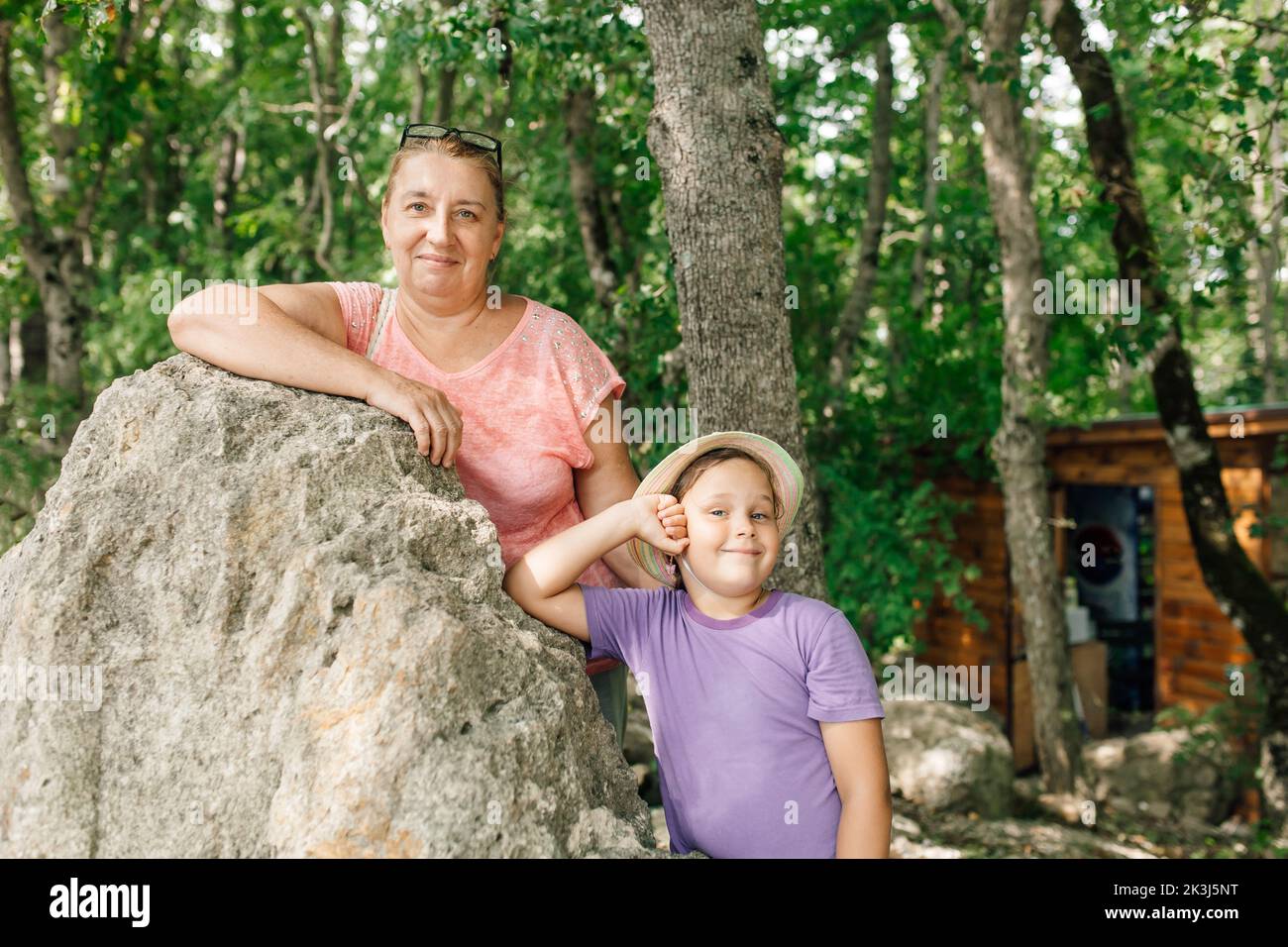 Adult mother and school aged daughter resting together in forest camp. Happy family walk and spend summer vacation in wild nature in mountains. Hiking Stock Photo