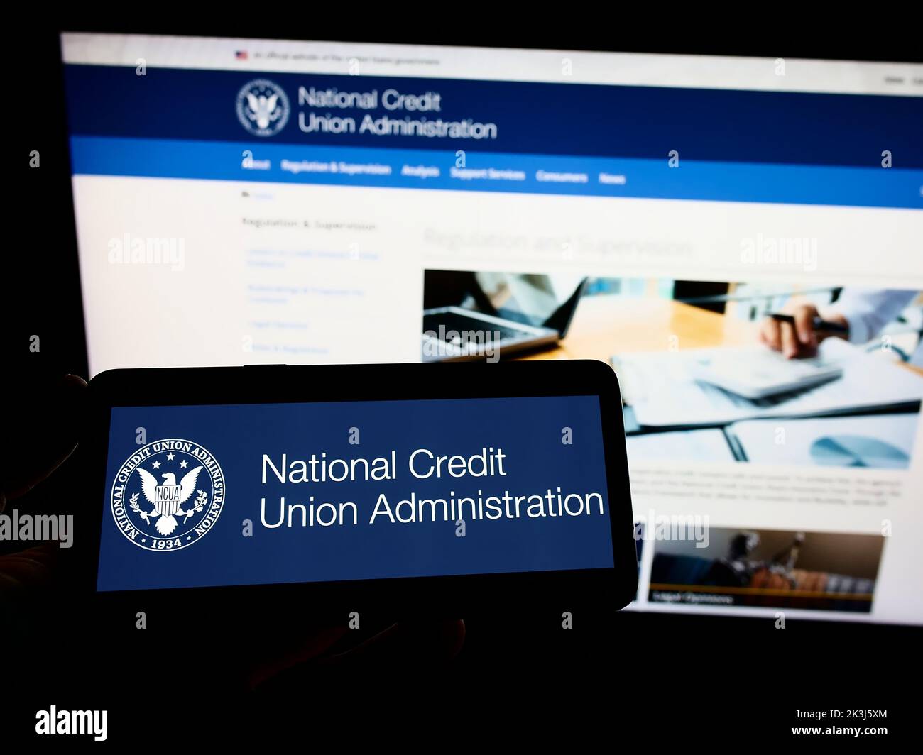 Person holding smartphone with logo of US National Credit Union Administration (NCUA) on screen in front of website. Focus on phone display. Stock Photo