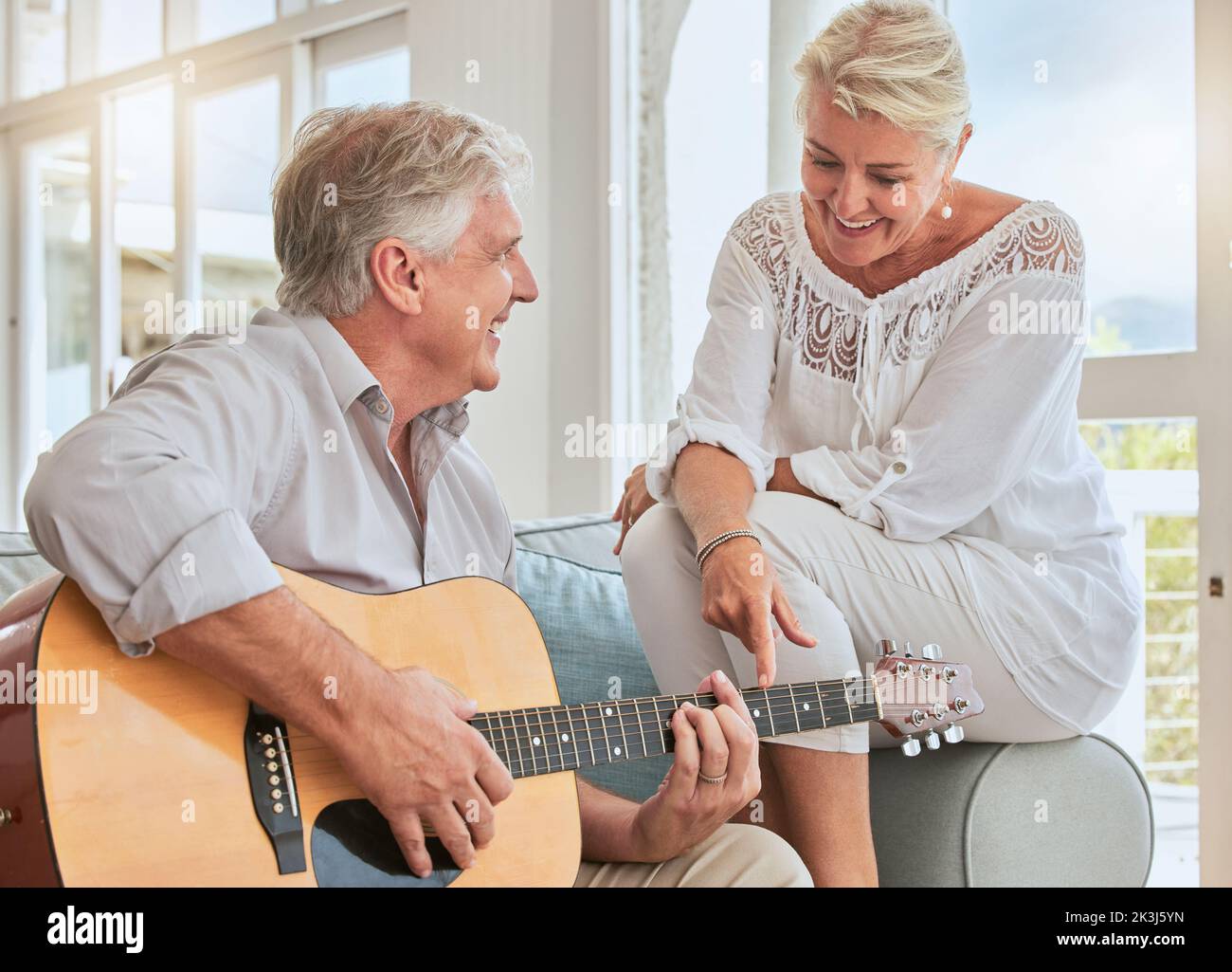 Old couple, guitar and love in home, sofa or couch playing a romantic, lovely or affection musical song for wife. Romance, retired senior man and Stock Photo