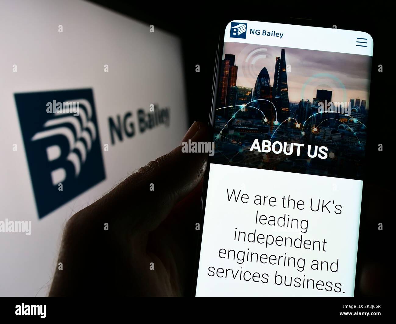 Person holding mobile phone with website of engineering company NG Bailey Group Limited on screen with logo. Focus on center of phone display. Stock Photo