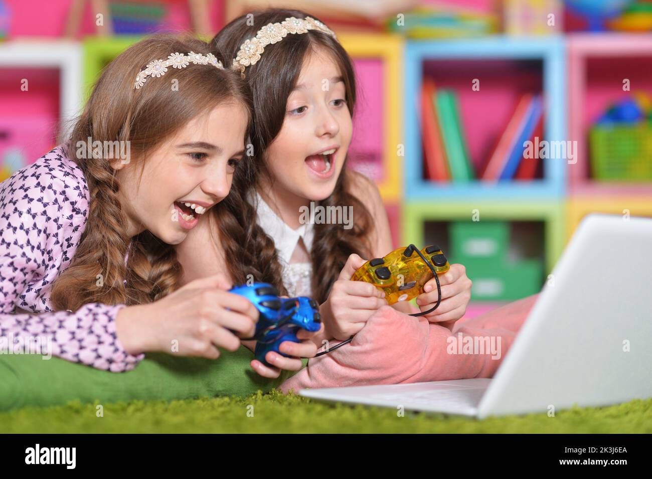 Portrait of two girls playing with joystick and laptop at home Stock Photo