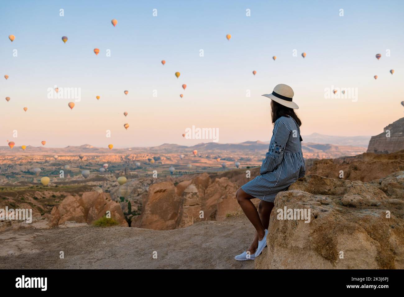Asian women watching the sunset in Cappadocia with hot air balloons in the sky during sunrise in Cappadocia Turkey. Kapadokya Gorem. Happy mid age women in a hot air balloon  Stock Photo