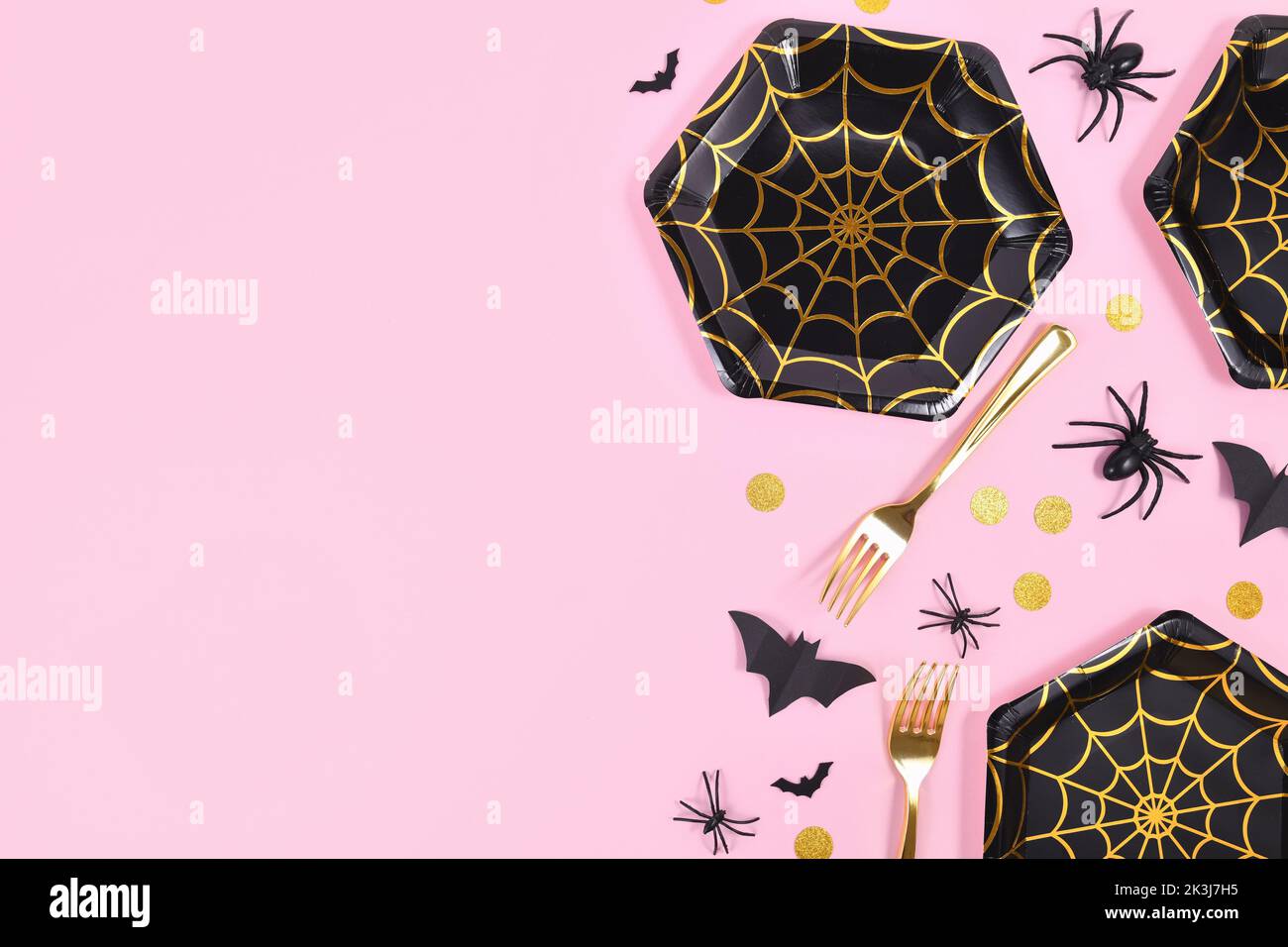 Halloween party flat lay with black and gold spider web plates, spiders and confetti on pink background Stock Photo