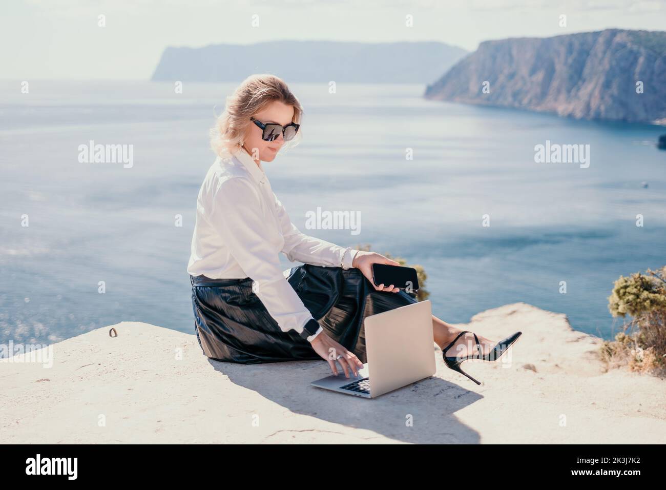 Digital nomad, Business woman working on laptop by the sea. Pretty lady typing on computer by the sea at sunset, makes a business transaction online Stock Photo