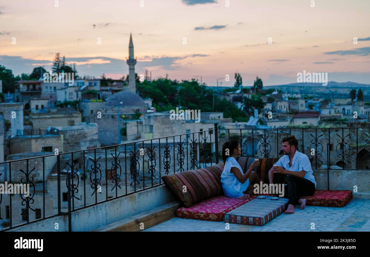 happy couple with a drink on the rooftop of a cave house historical village of Ayvali Goreme Cappadocia, couple watch sunset Kapadokya.  Stock Photo