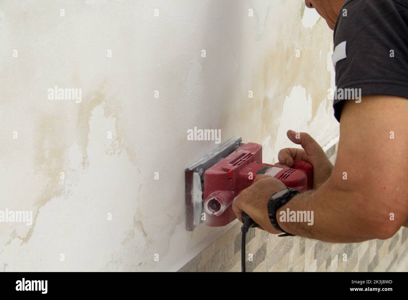 A handyman removing plaster and mold from a wall with a sanding machine Stock Photo