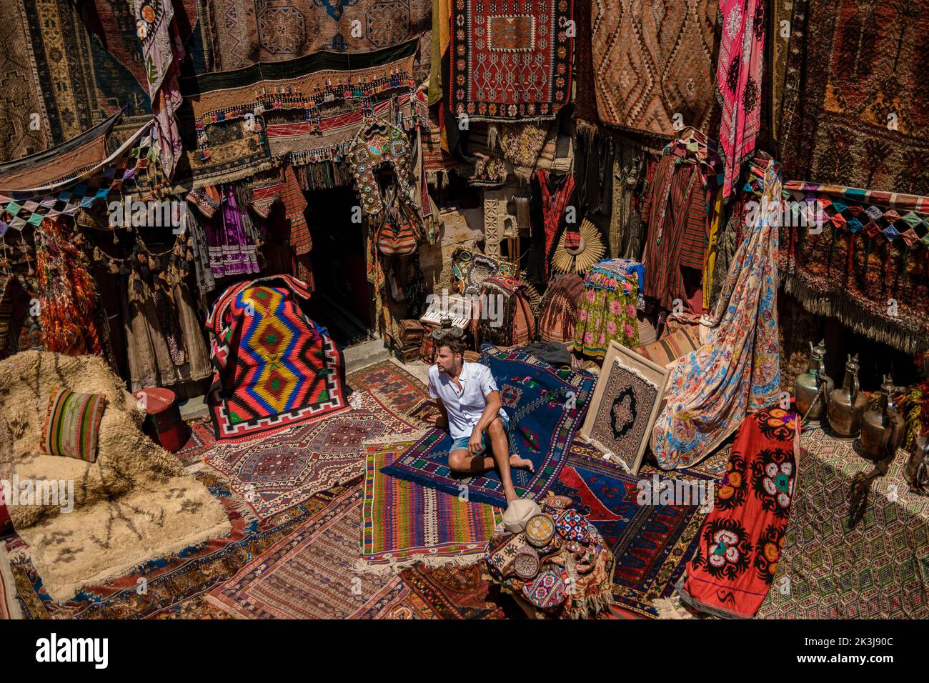 young man tourist at an old traditional Turkish carpet shop in cave house Cappadocia, Turkey Kapadokya. Colorful carpet shop in Goreme Stock Photo