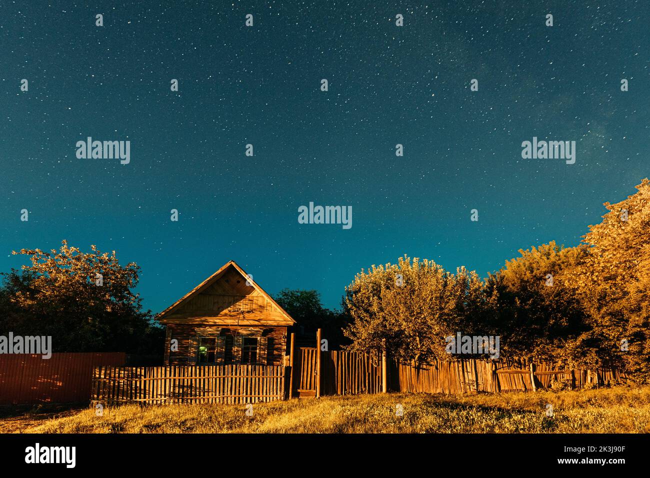 Night sky over house in old village. Night starry sky above house with bright stars and meteoric track trail. Glowing stars above summer nature Stock Photo