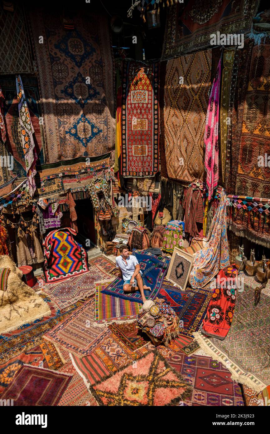 young man tourist at an old traditional Turkish carpet shop in cave house Cappadocia, Turkey Kapadokya. Colorful carpet shop in Goreme Stock Photo