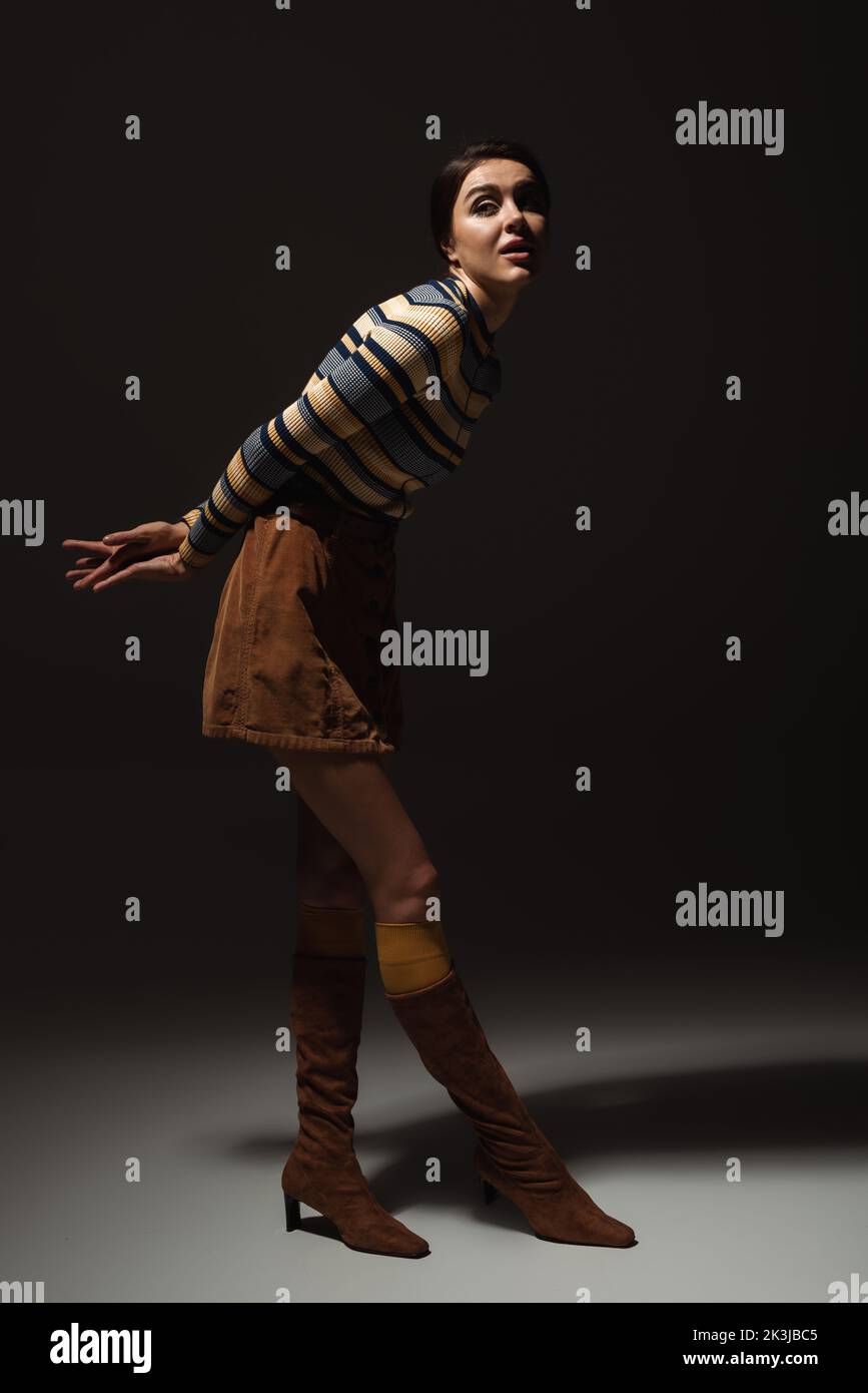 full length of young model in striped turtleneck with skirt and boots posing on black,stock image Stock Photo