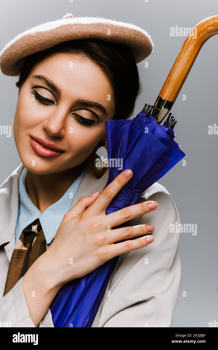 portrait of brunette woman in beret and coat posing with bright blue ...