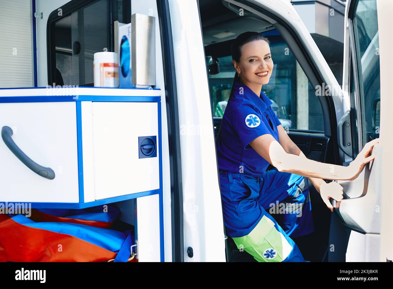 Portrait of caucasian woman paramedic sitting in a modern ambulance near hospital emergency room. Emergency medical services Stock Photo