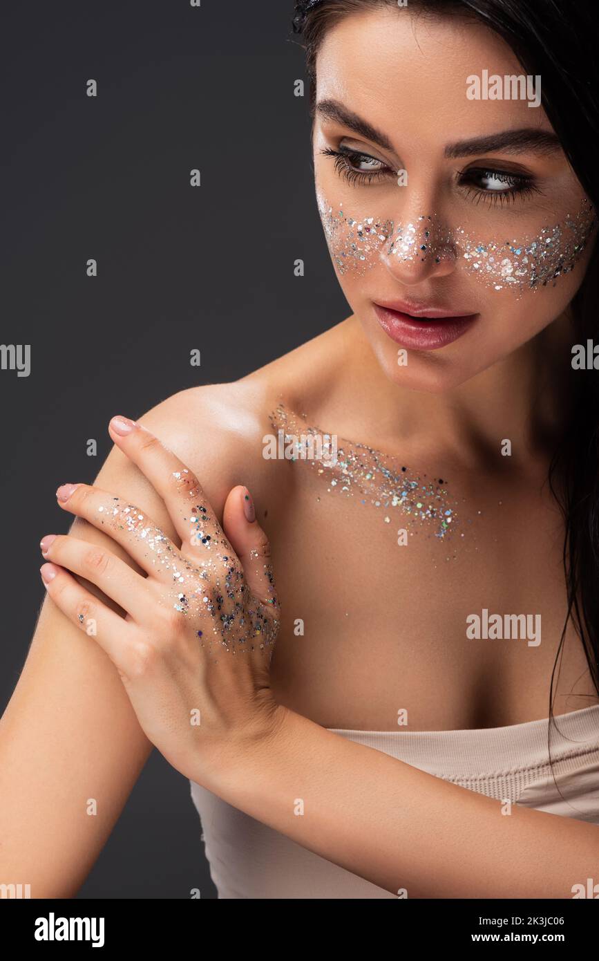 portrait of woman with natural makeup and sparkling glitter on face and body touching bare shoulder isolated on grey,stock image Stock Photo