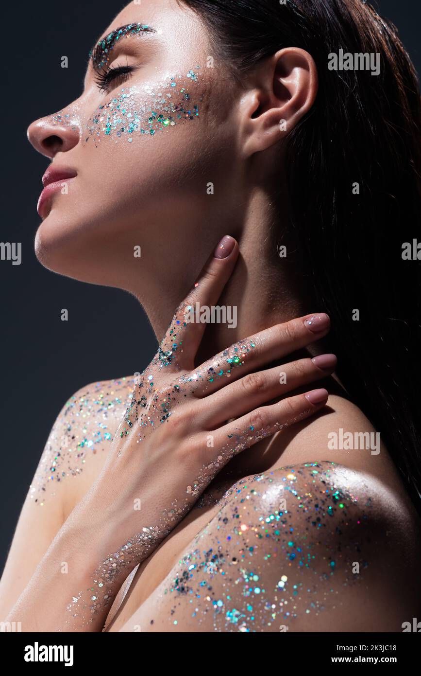 portrait of young woman with closed eyes and glitter on eyebrows touching neck isolated on grey,stock image Stock Photo