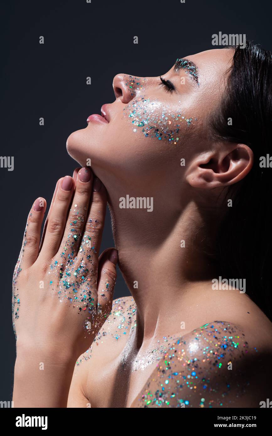 side view of young woman with closed eyes and glitter on face praying isolated on grey,stock image Stock Photo