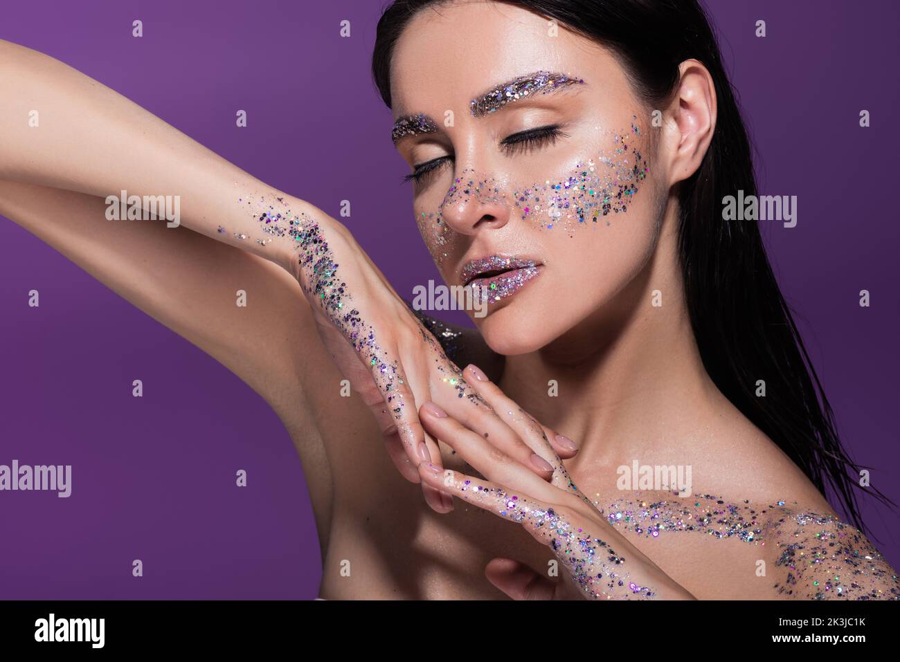 sensual woman with closed eyes and glitter on face posing isolated on purple,stock image Stock Photo