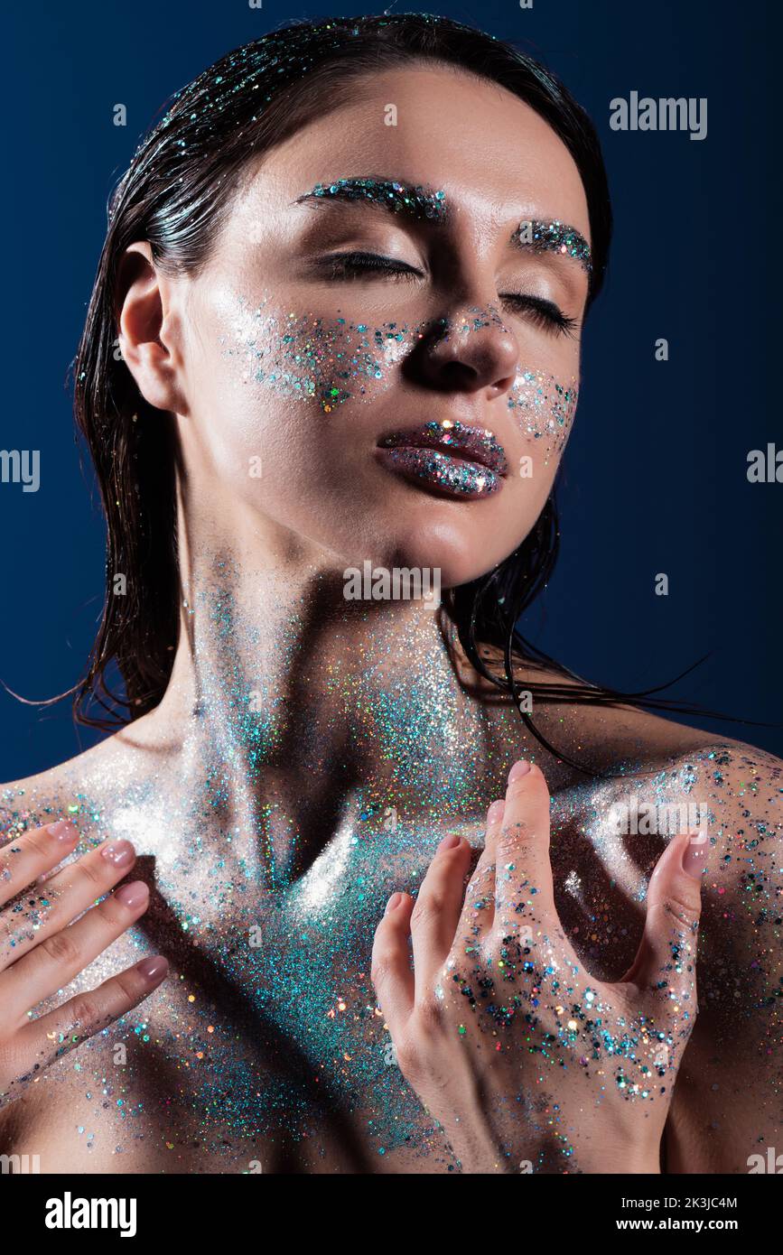 portrait of young woman with closed eyes and sparking glitter on body isolated on blue,stock image Stock Photo