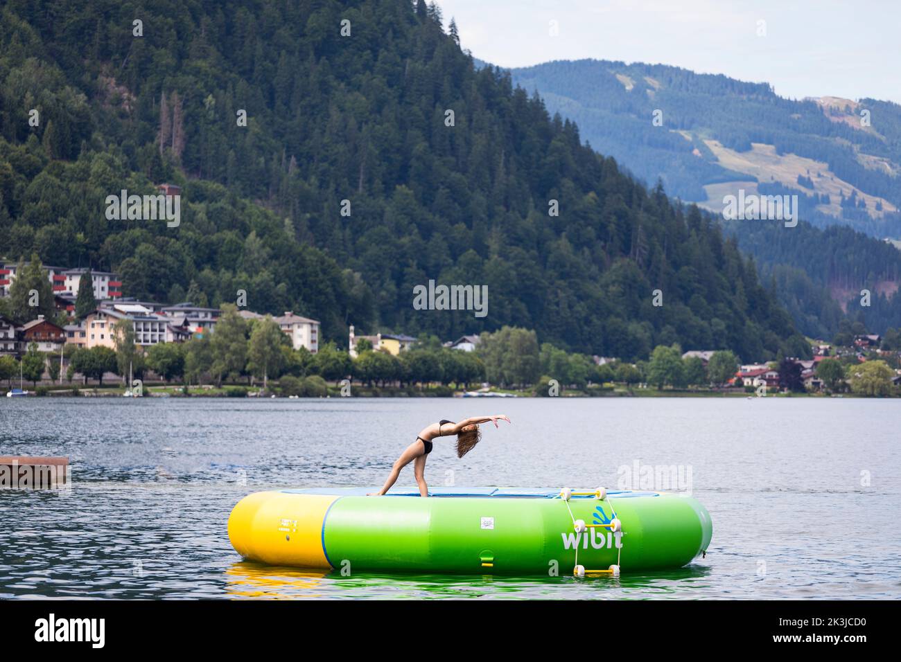 Sportive young girl performs a pedanitos at a floating trampoline in the lake at Zell am See, Austria Stock Photo