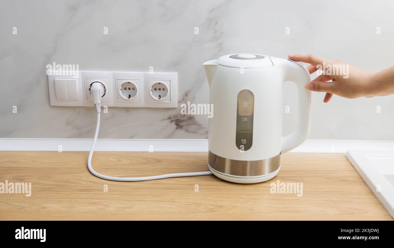 A woman turns on an electric kettle to boil water in the kitchen