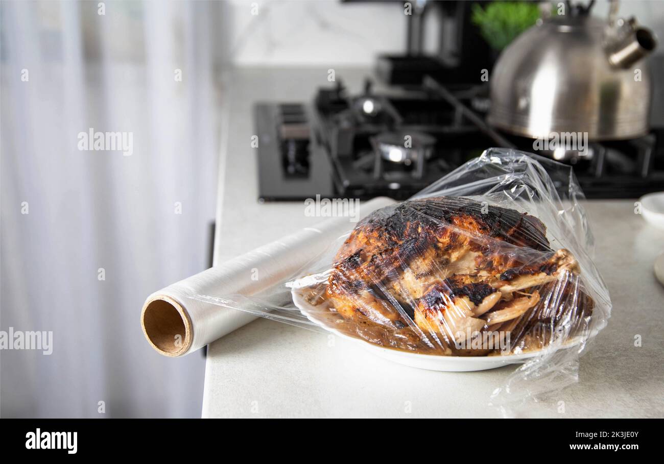 A plate with fried chicken wrapped in cling film in the kitchen, close