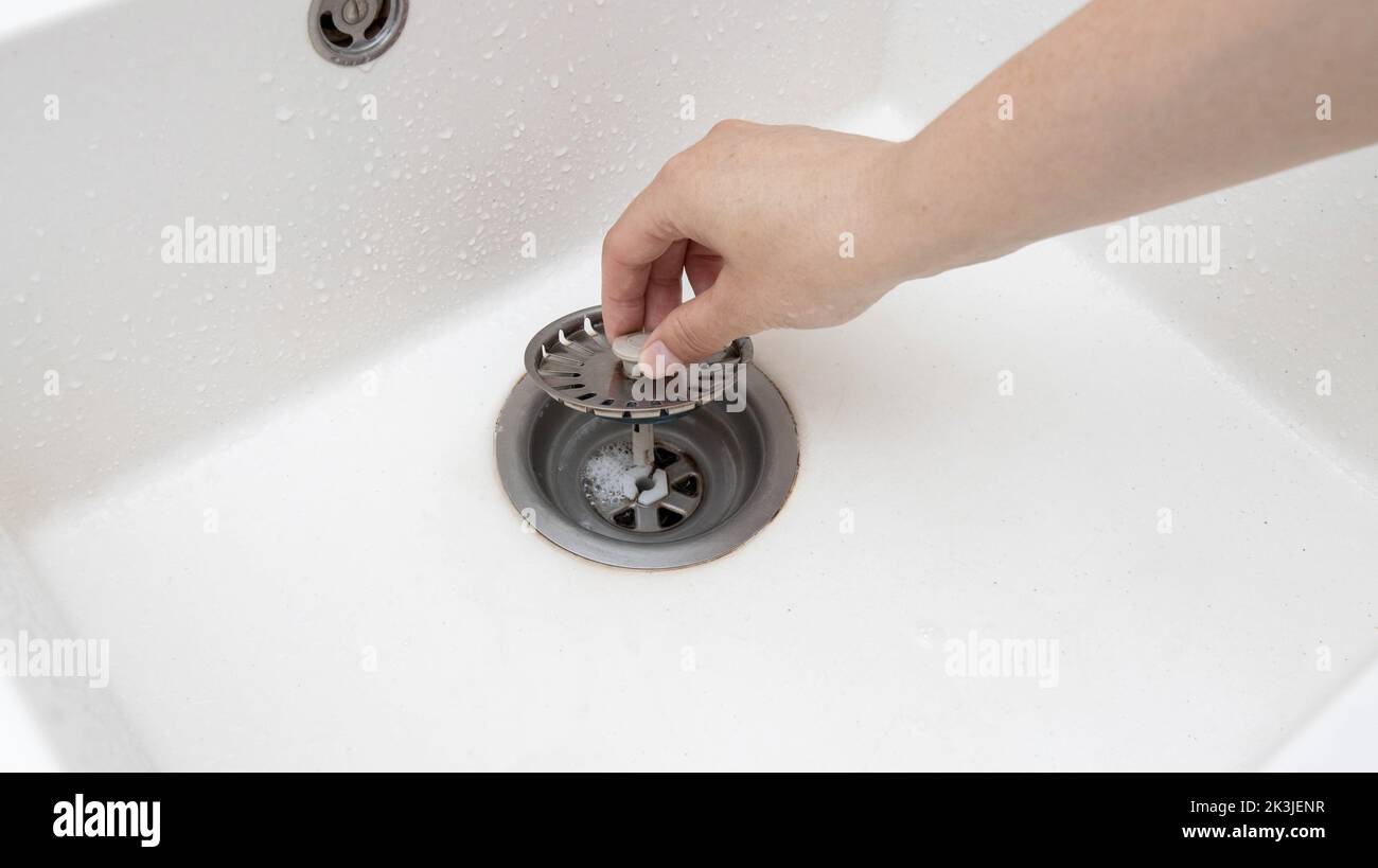 A man's hand removes a metal strainer from a kitchen sink drain
