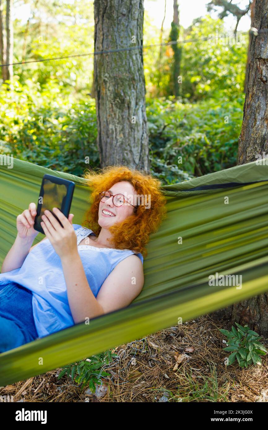 A woman shopping online for Black Friday from the comfort of a hammock Stock Photo