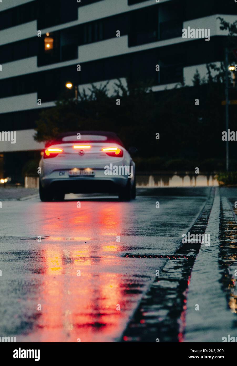 Cars taillight reflecting in the water / rain on the ground. Curb serves as guidline. Mood is gloomy and the picture looks cinematic. It's evening. Stock Photo