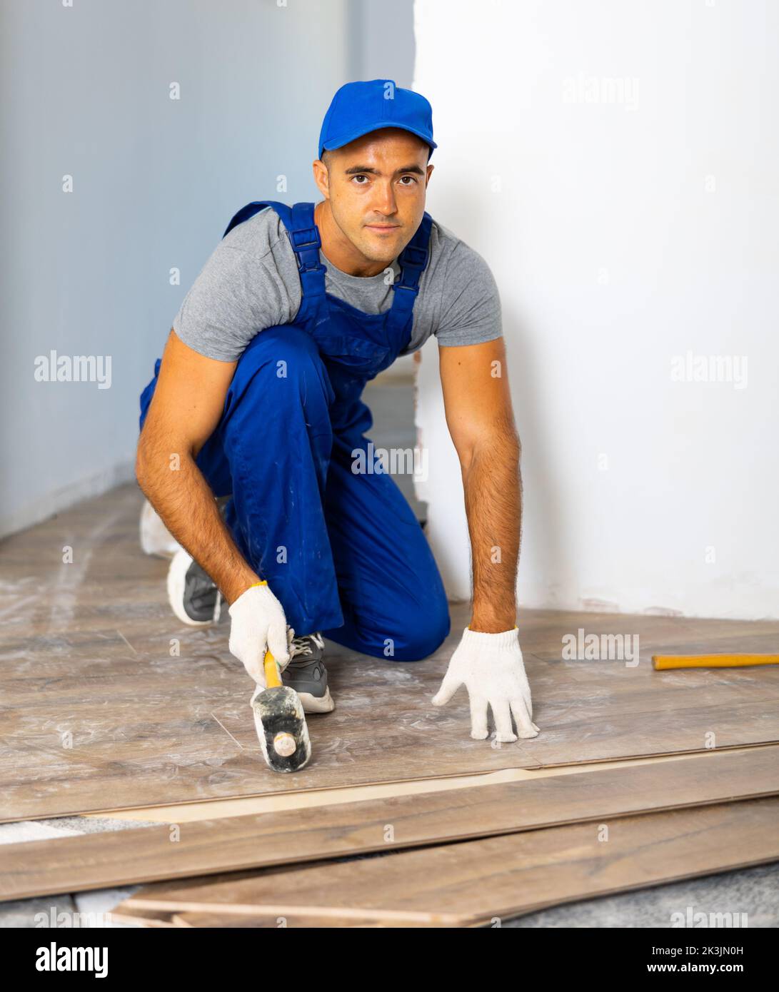 Handyman worker in work clothes use rubber hammers installing laminate