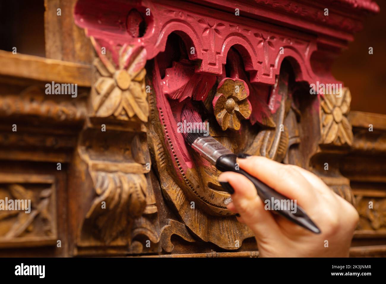 Coloring detailed carved ornaments of old wooden sideboard buffet with brush in pink color with female hand in foreground. New life of old things Stock Photo