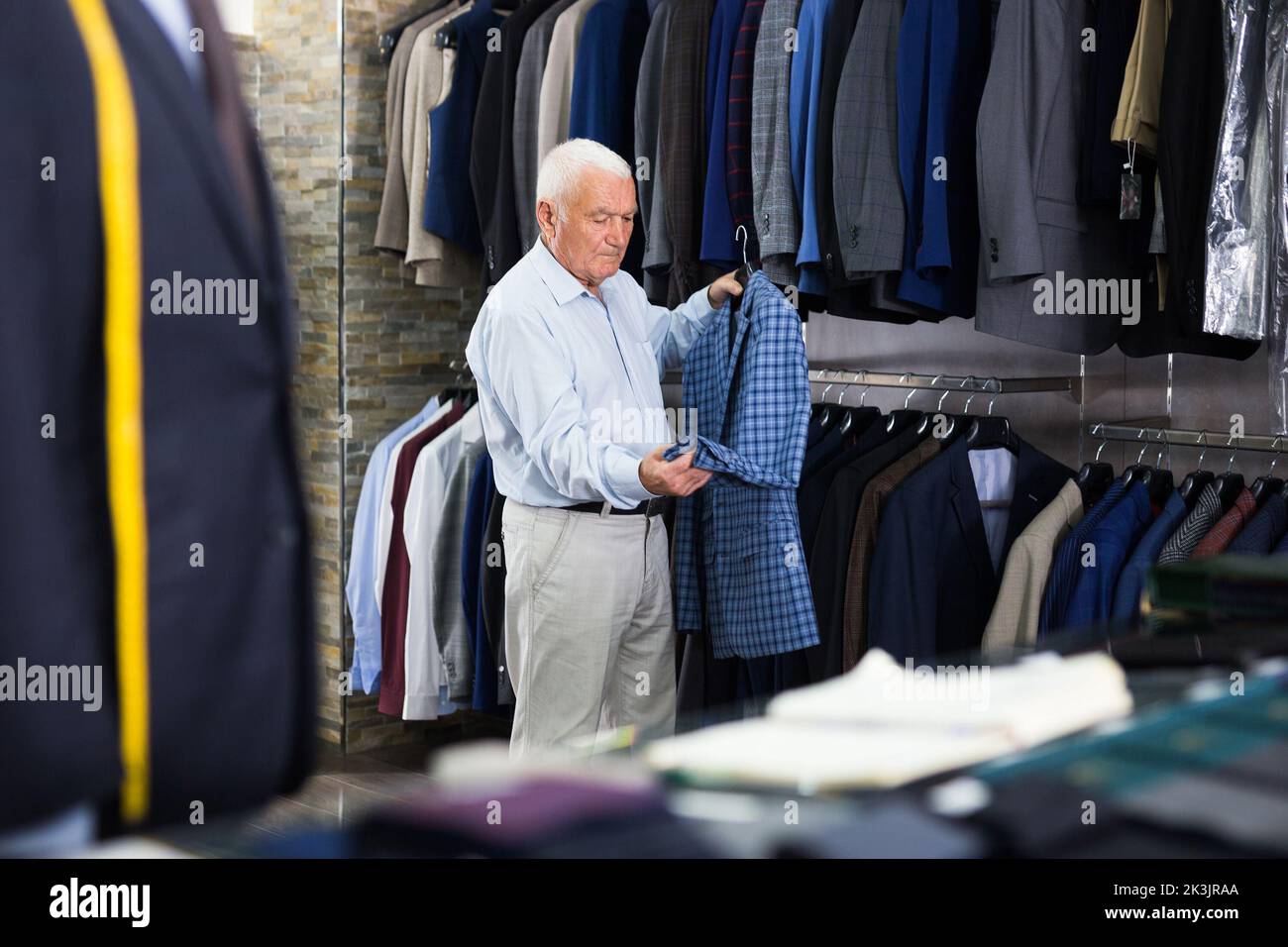 Senior citizen chooses fashionable plaid jacket in clothing store Stock Photo