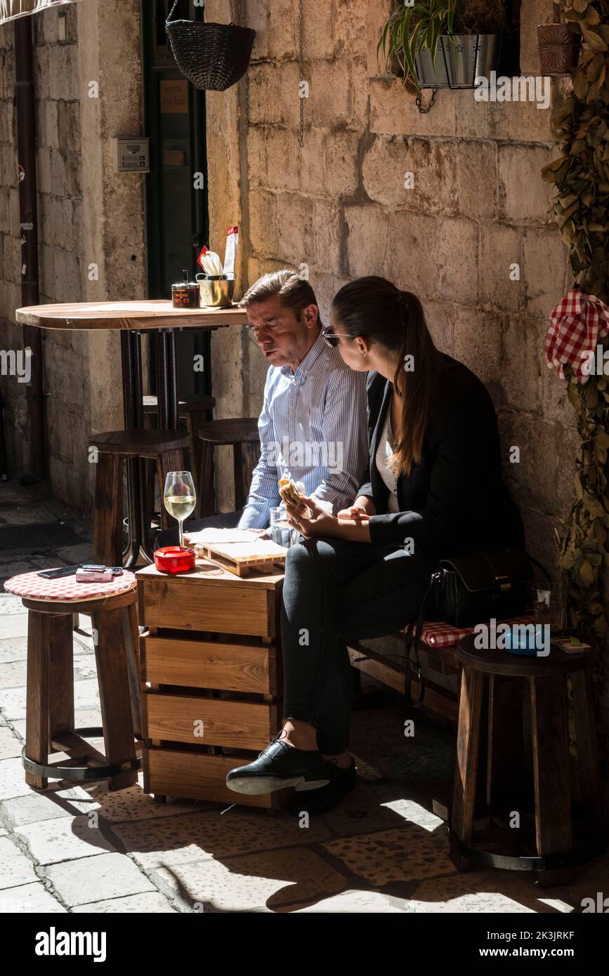 Tourist couple enjoying a small snack and a glass of white wine on a tiny terrace in the sunshine, Old town of Dubrovnik, Croatia. Stock Photo