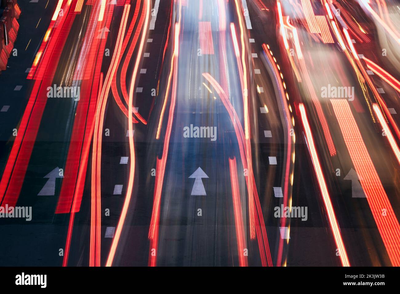 Light trails of cars on urban road during evening traffic jam. Illuminated arrows of road marking. Stock Photo