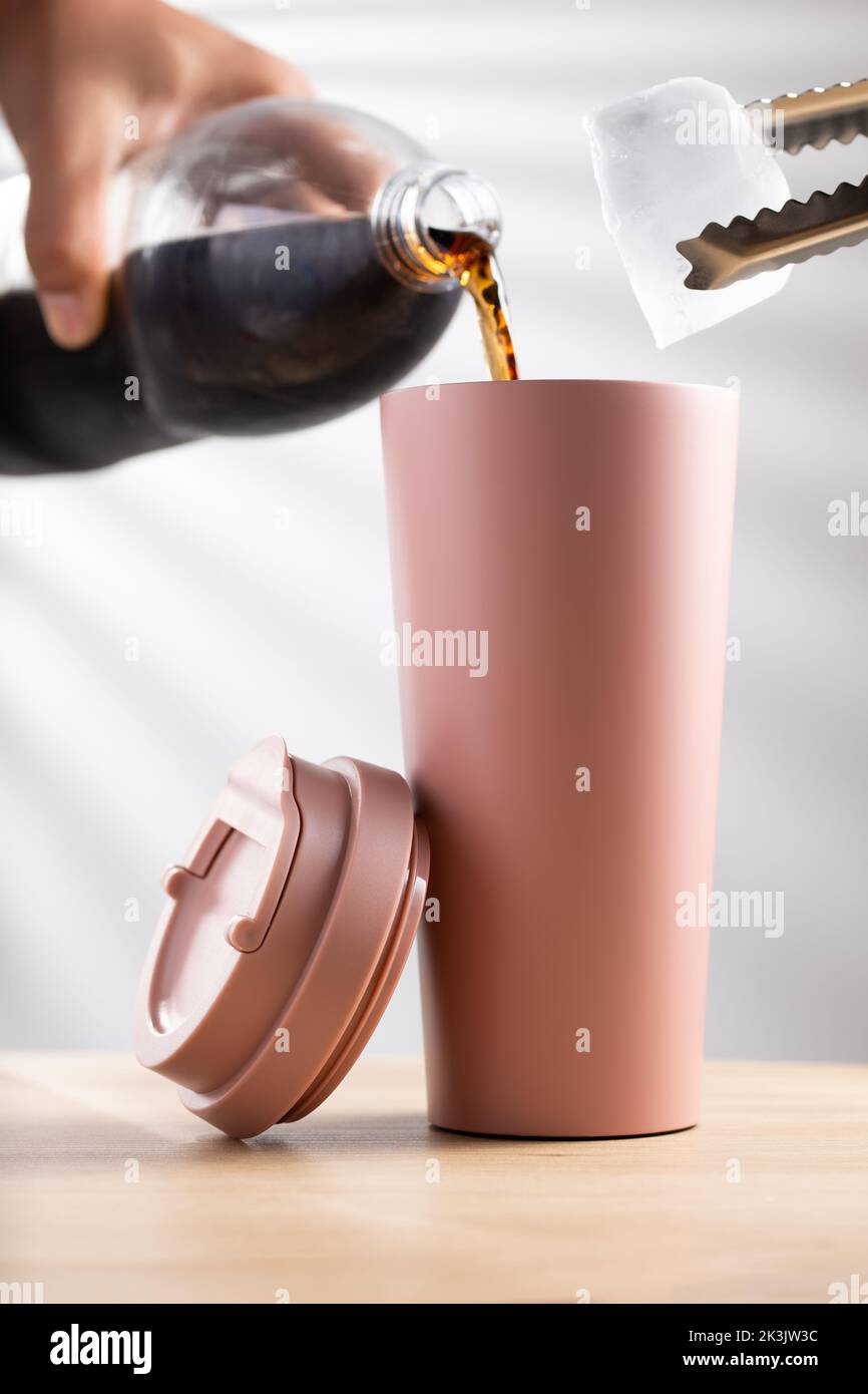 Putting soft drink and ice cube into a pastel pink tumbler size 20