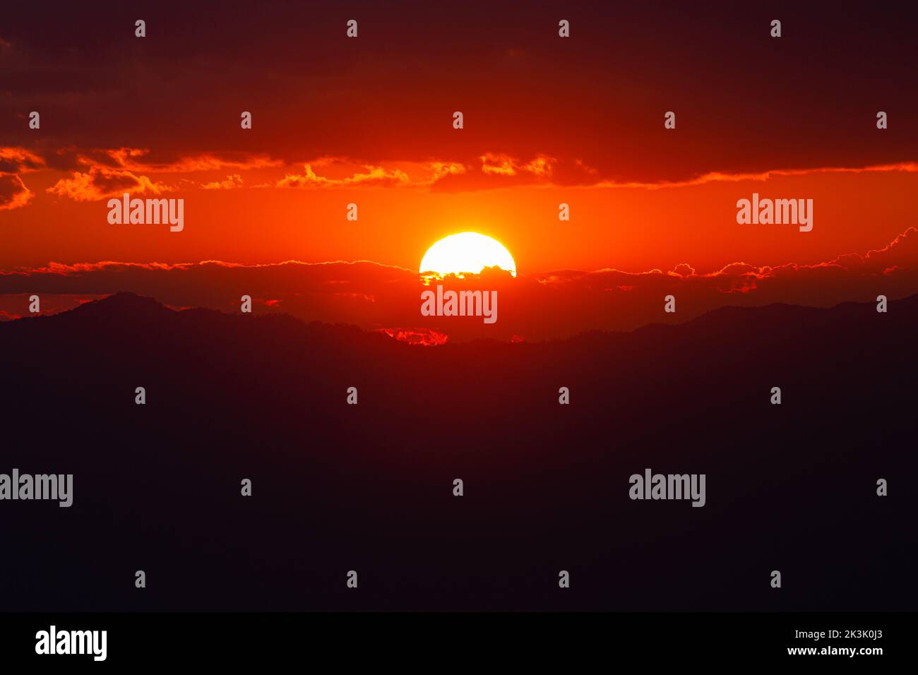 Red light from sun shining through overcast sky at sunset Stock Photo