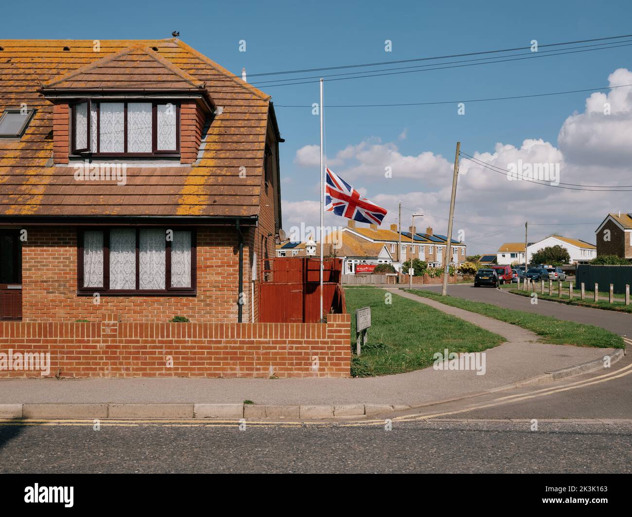A UK Union Flag flies at half mast in mourning for the Queen's passing in a suburban residential housing estate Lydd, Sussex, England, UK - Sept 2022 Stock Photo