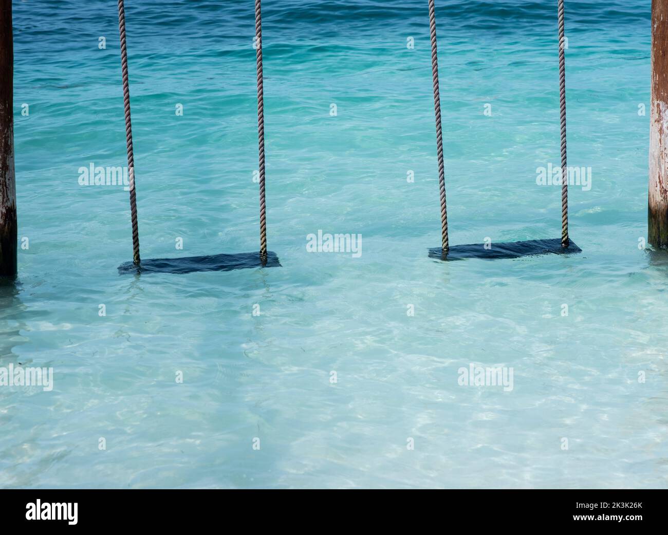 Two empty swings on the water by the sea at a tropical beach. Vacation travel concept Stock Photo