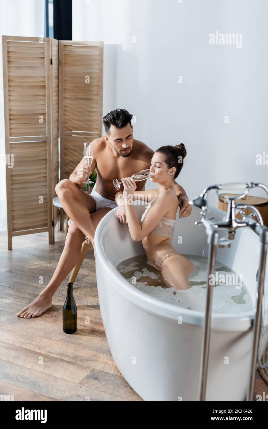 seductive woman drinking champagne in bathtub near boyfriend in underpants Stock Photo