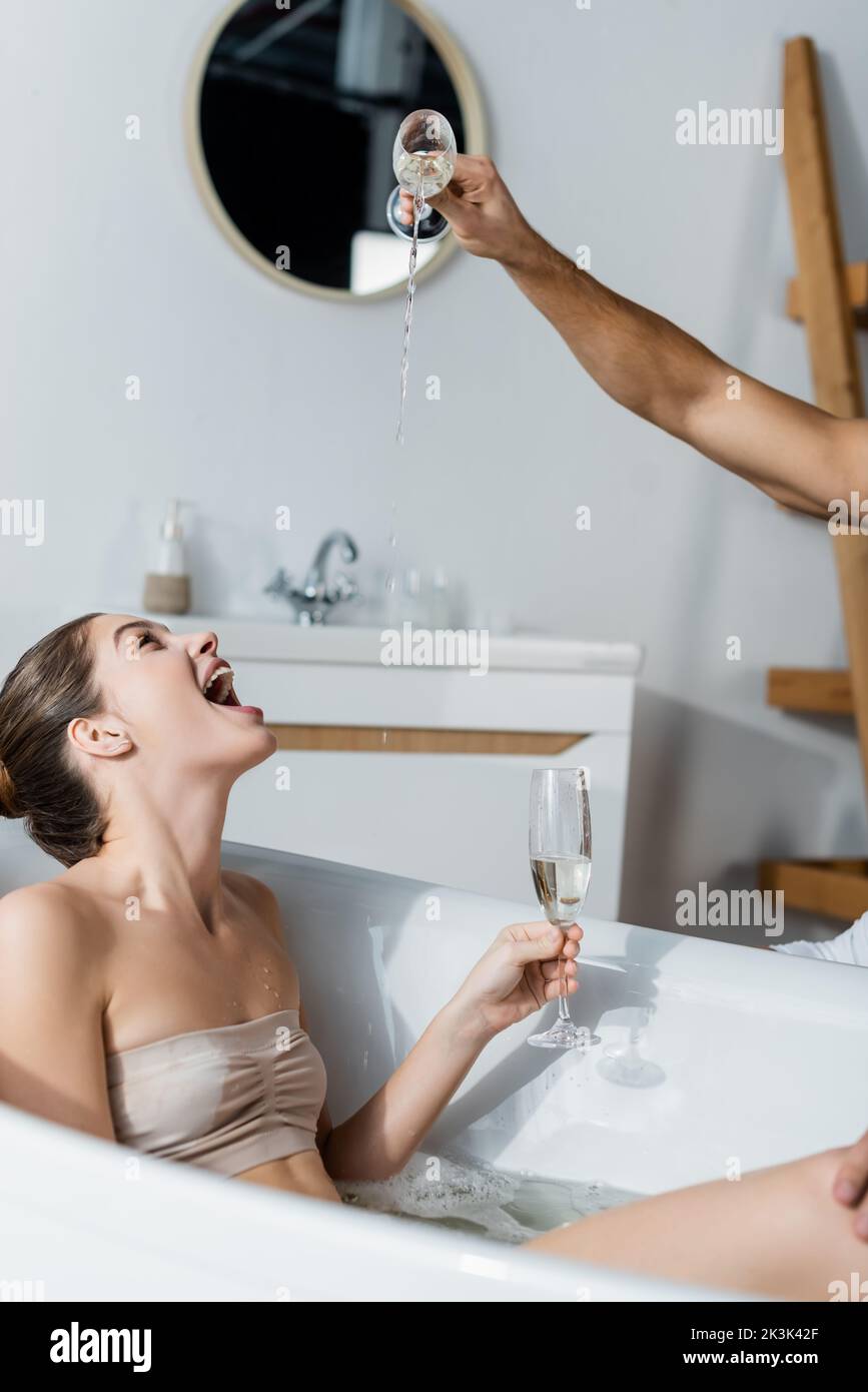 man pouring champagne near amazed young woman in bathtub Stock Photo