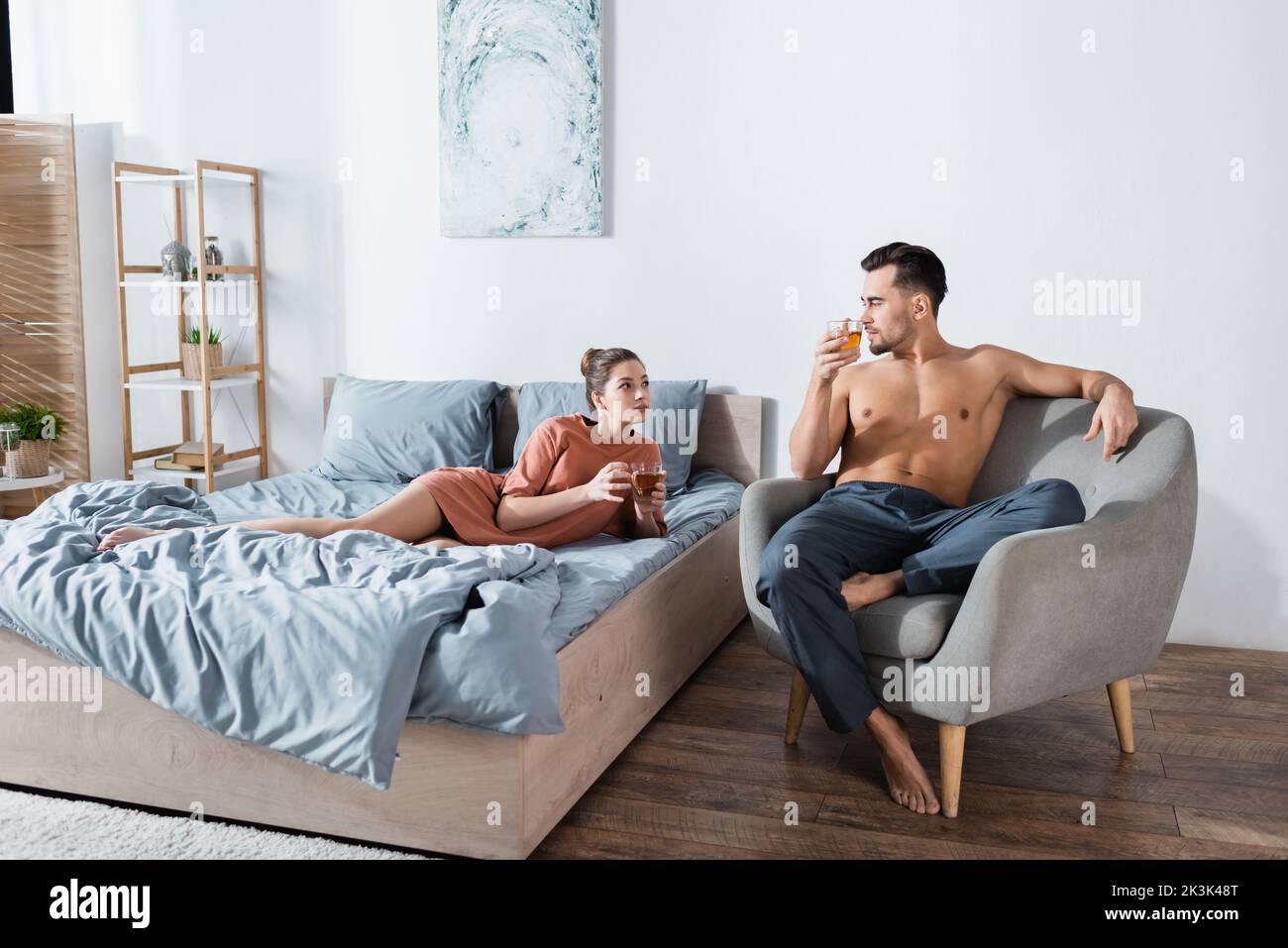 young couple looking at each other while drinking tea in modern bedroom Stock Photo