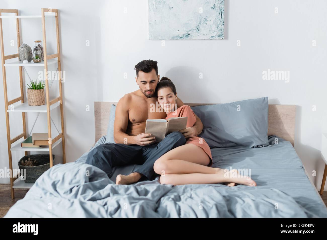 young and sexy couple reading book on grey bedding at home Stock Photo