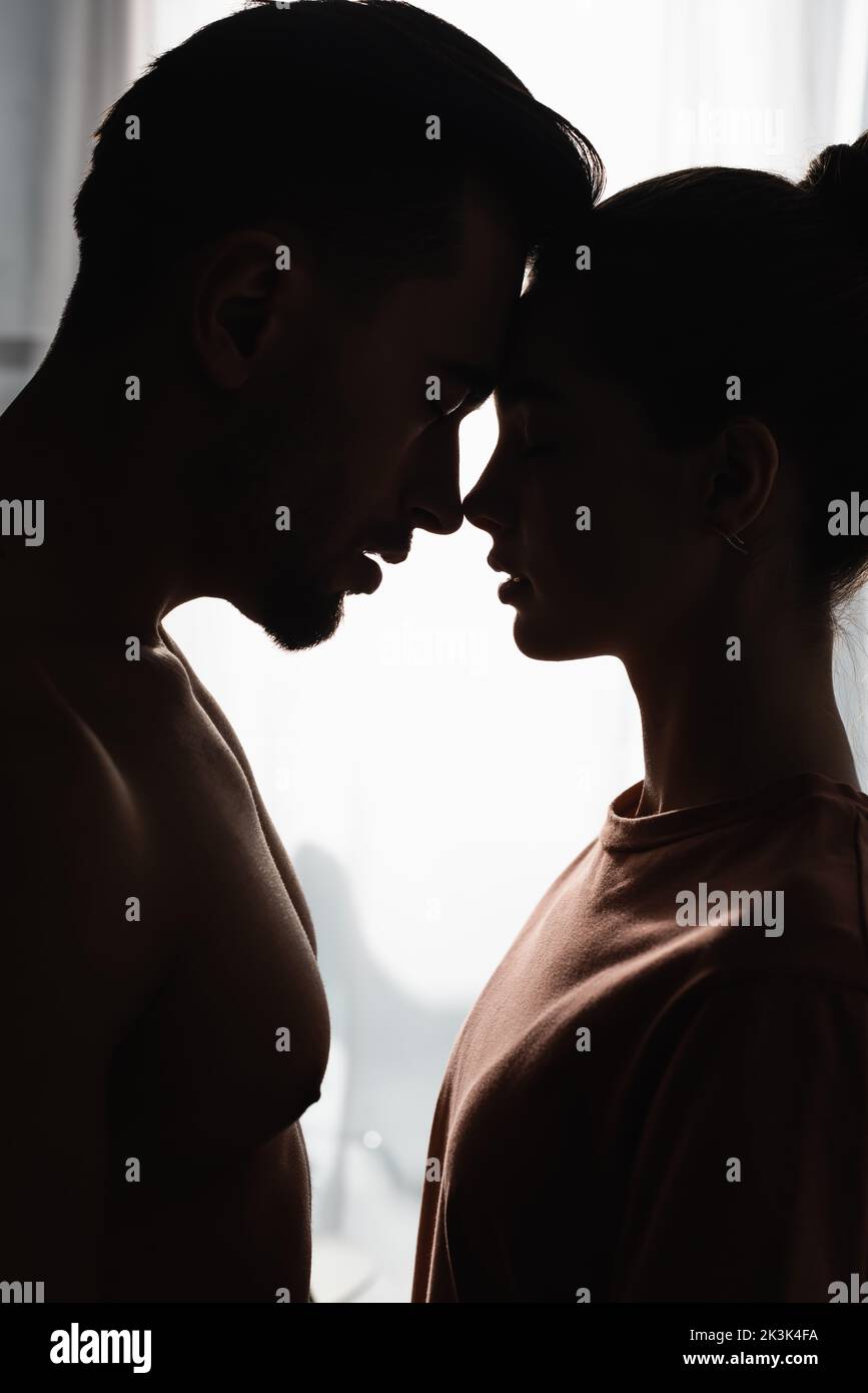 side view of silhouettes of woman in t-shirt and shirtless man standing face to face with closed eyes Stock Photo