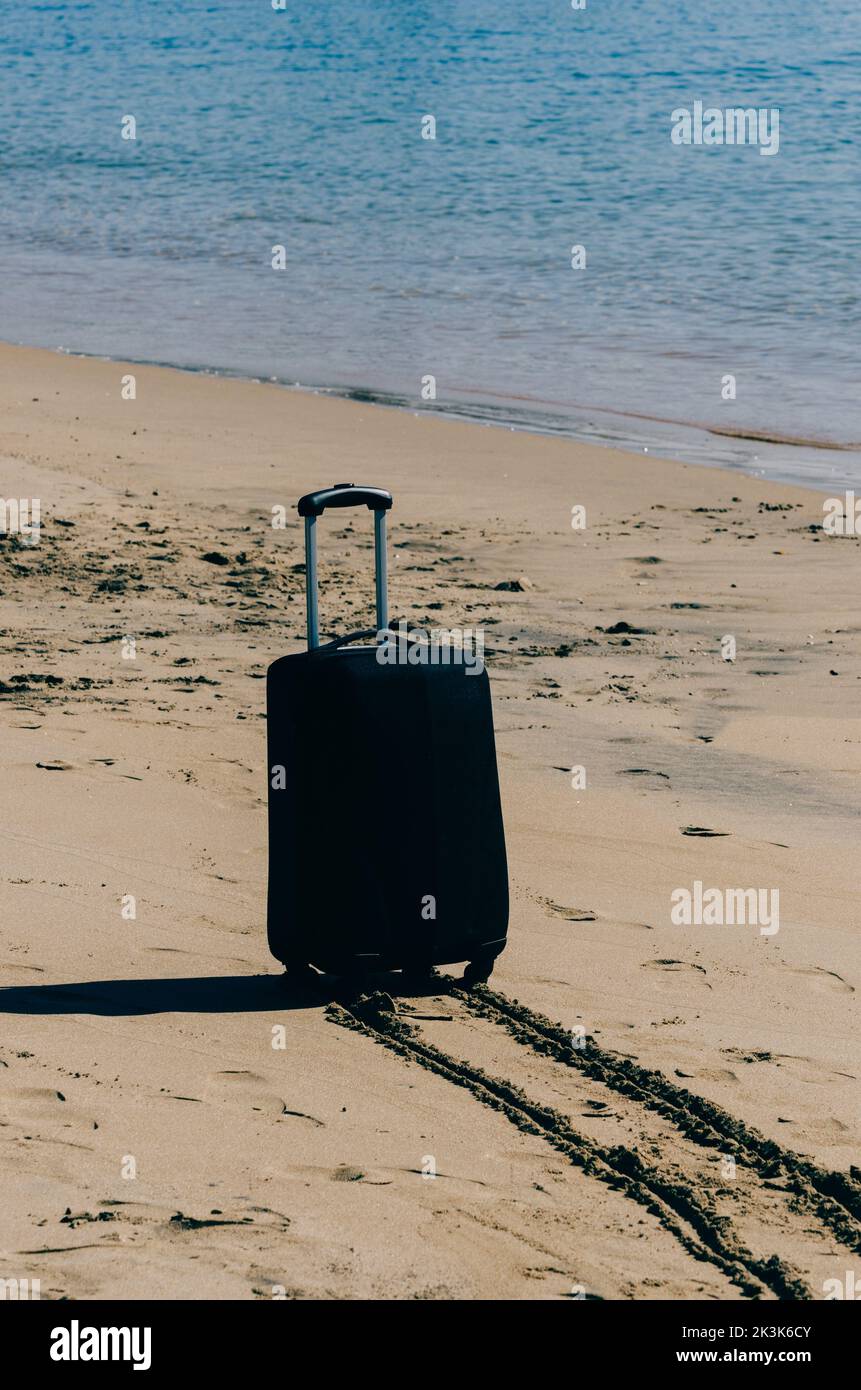 Black travel suitcase on sandy beach with turquoise sea background, summer holidays concept Stock Photo