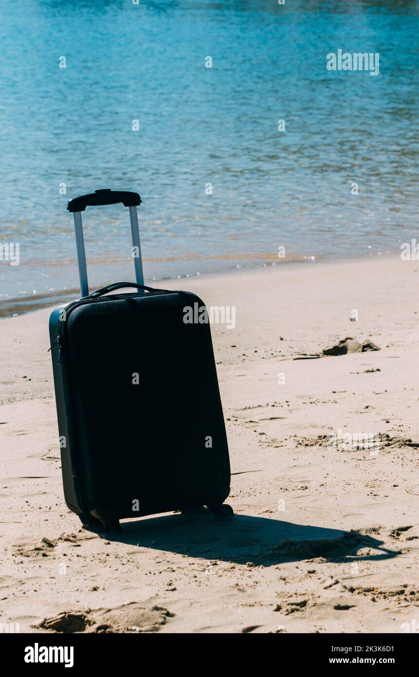 Black travel suitcase on sandy beach with turquoise sea background, summer holidays concept Stock Photo
